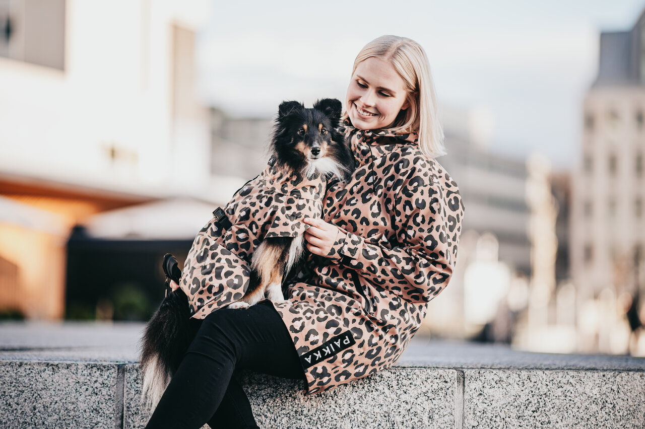 PAIKKA-Regenmantel-fuer-Zweibeiner-reflektierend-Human-Visibility-Raincoat-Leo-Damen-blonde-Frau-mit-Hund-am-Schoss-60-46253 PAIKKA-Regenmantel-fuer-Zweibeiner-reflektierend-Human-Visibility-Raincoat-Leo-Damen-blonde-Frau-mit-Hund-am-Schoss-60-46253